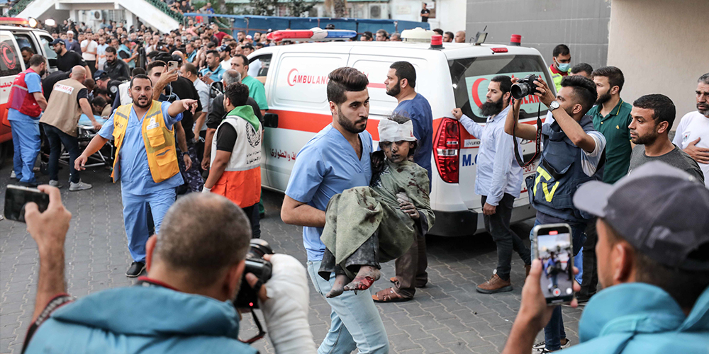 ممرض يقوم بحمل طفلة مُصابة في مستشفى الشفاء الطبي في غزة